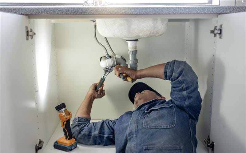 Plumber repairing pipes beneath a bathroom sink in Carlisle