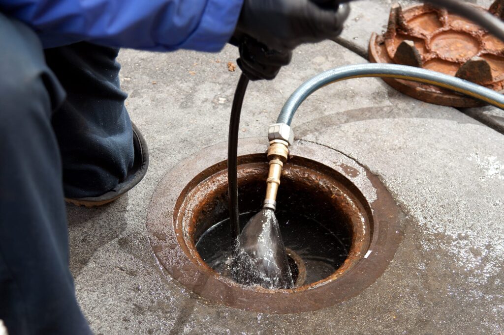 Plumber hydro jetting a sewer line through a manhole in Carlisle
