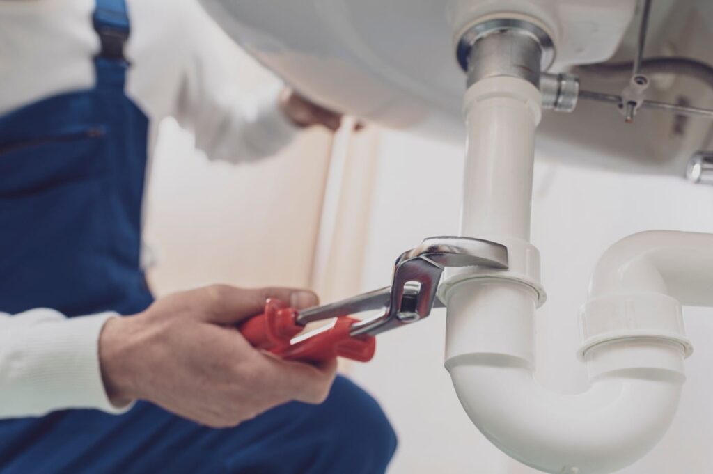 Plumber repairing a white drain pipe beneath a sink in Carlisle