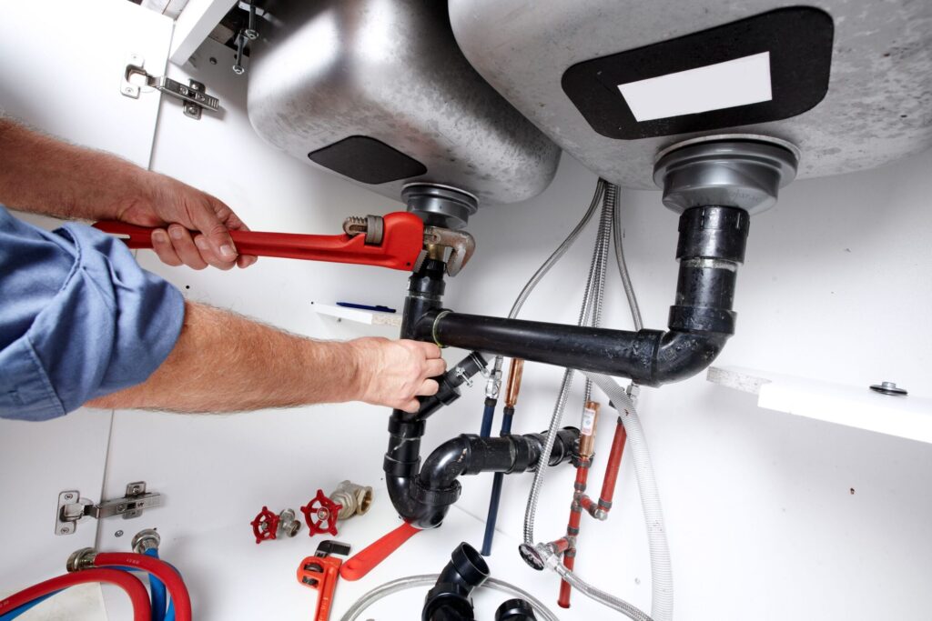 Plumber repairing drain pipes beneath a kitchen sink in Carlisle